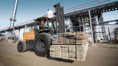 man driving a forklift in a construction site carrying wood planks